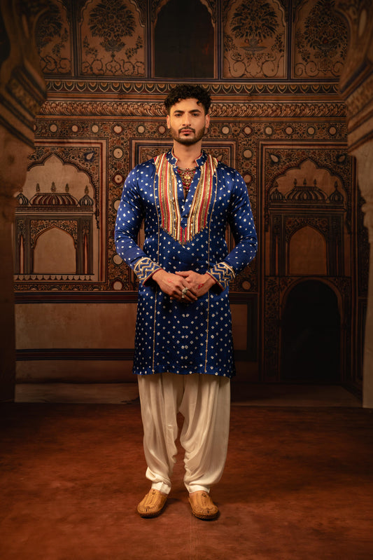 Man wearing a blue traditional outfit with white pants in an ornate room.