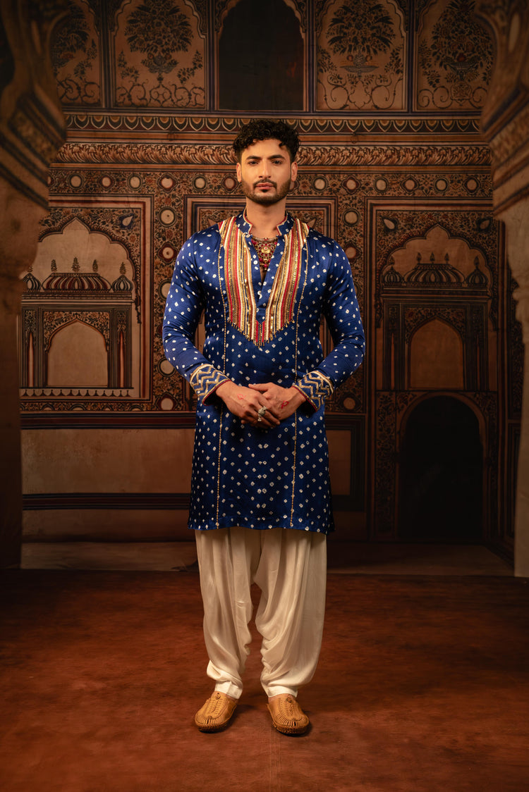 Man wearing a blue traditional outfit with white pants in an ornate room.