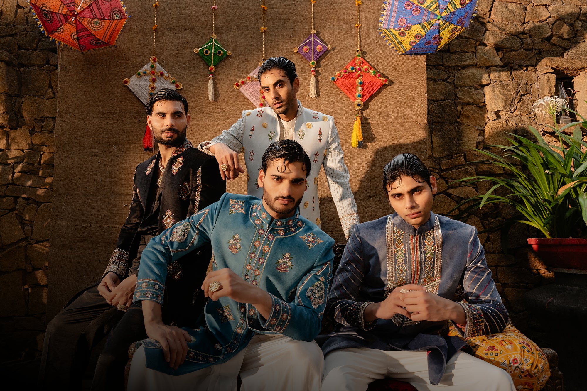 Four men in traditional attire sitting together with decorative items in the background.