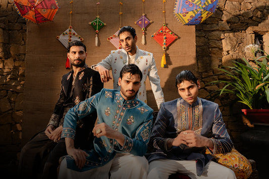 Four men in traditional attire sitting together with decorative items in the background.